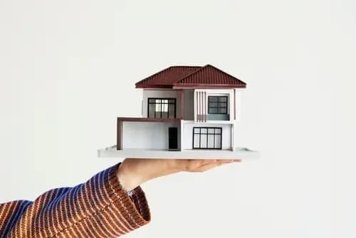 A model house held in an open hand, representing property ownership decisions